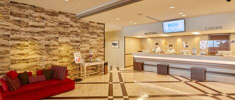 A hotel reception area with a red sofa, a reception desk, and a wall with a marble-like pattern.