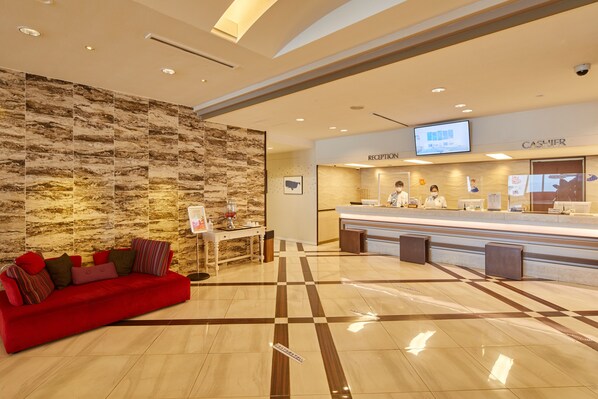 Zona de recepción de un hotel con un sofá rojo, un mostrador de recepción y una pared con diseño que imita el mármol.