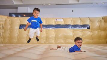 Two children playing on a large, padded, yellow wall.