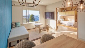 Habitación moderna con un ventanal grande, una cama con televisor, una zona de comedor y un área de estar con vistas.