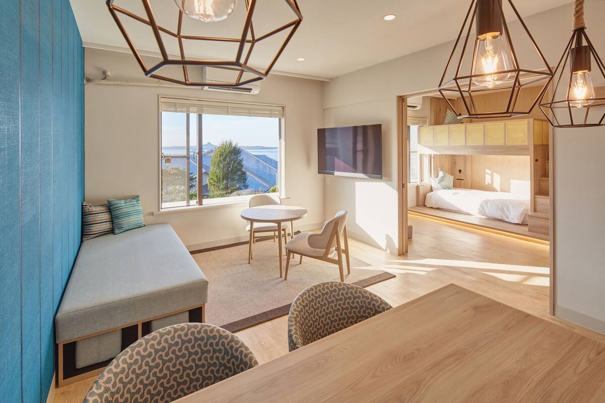 A modern room with a large window, a bed with a TV, a dining area, and a seating area with a view.