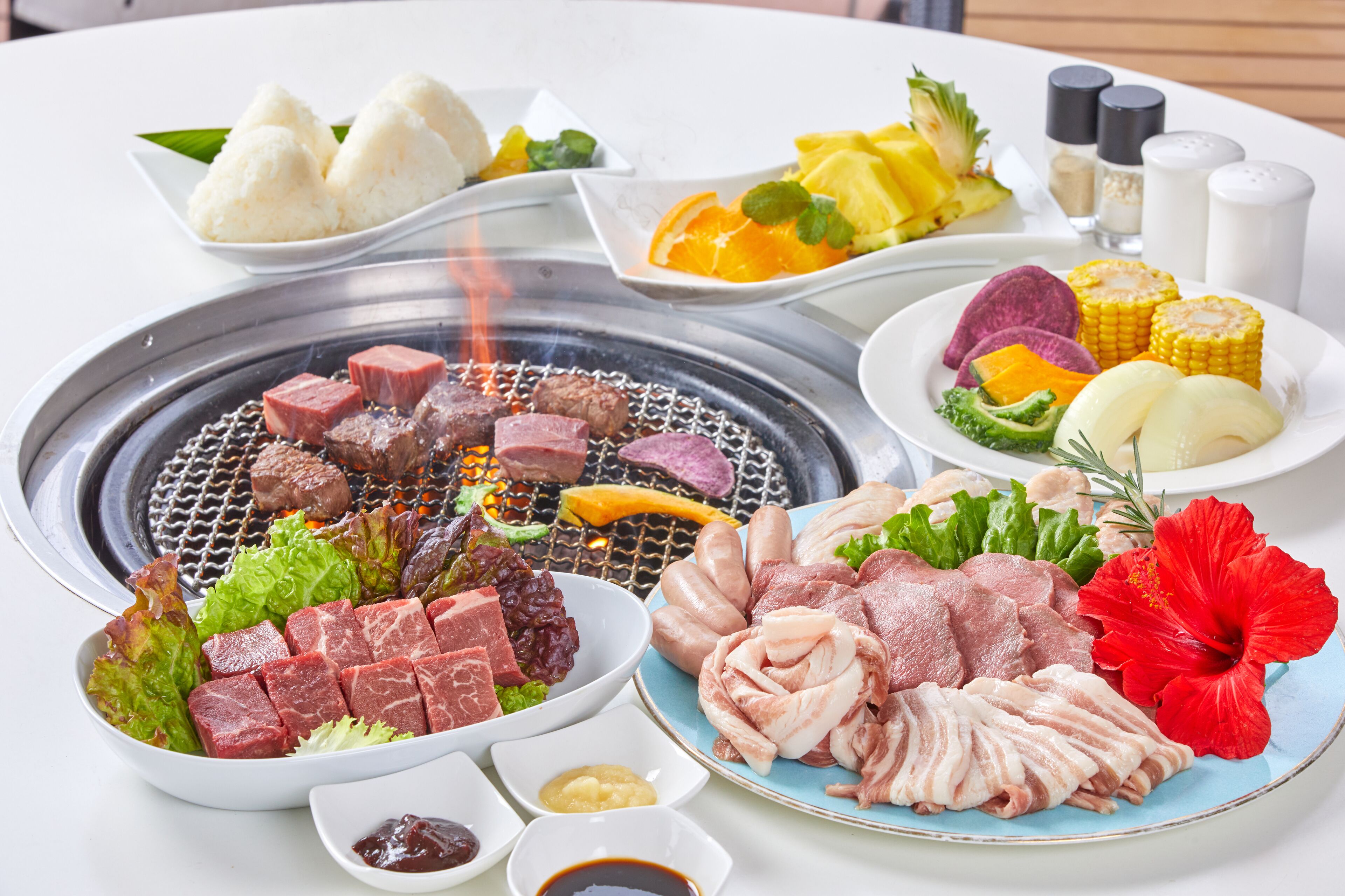 A variety of dishes including meat, vegetables, and dumplings, served on a table with a hot grill.