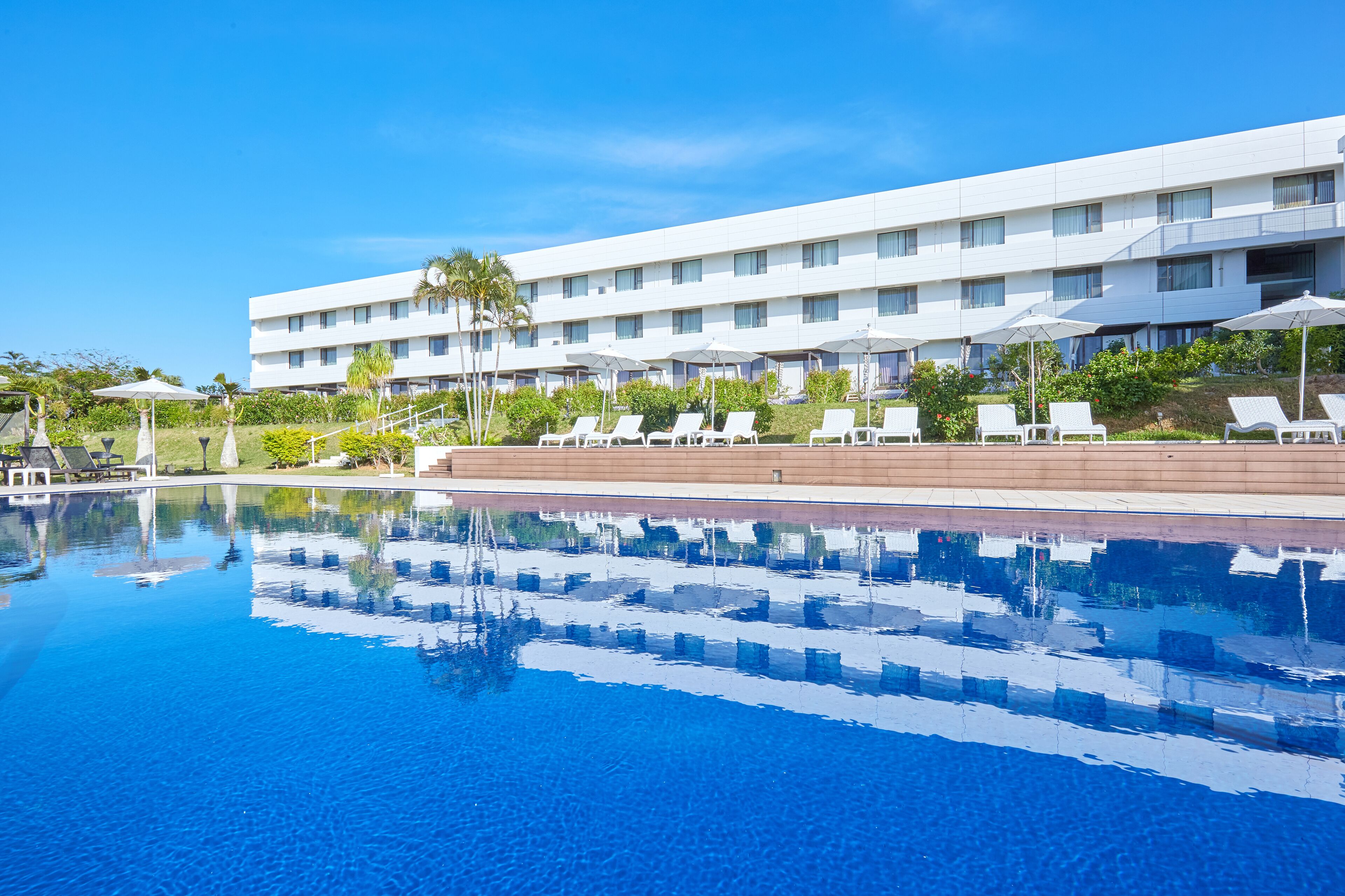 Un hotel con piscina, tumbonas y fachada de edificio blanca.