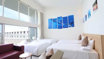 Una habitació d'hotel amb dos llits, un sofà vermell, una taula rodona petita i obra d'art a la paret.