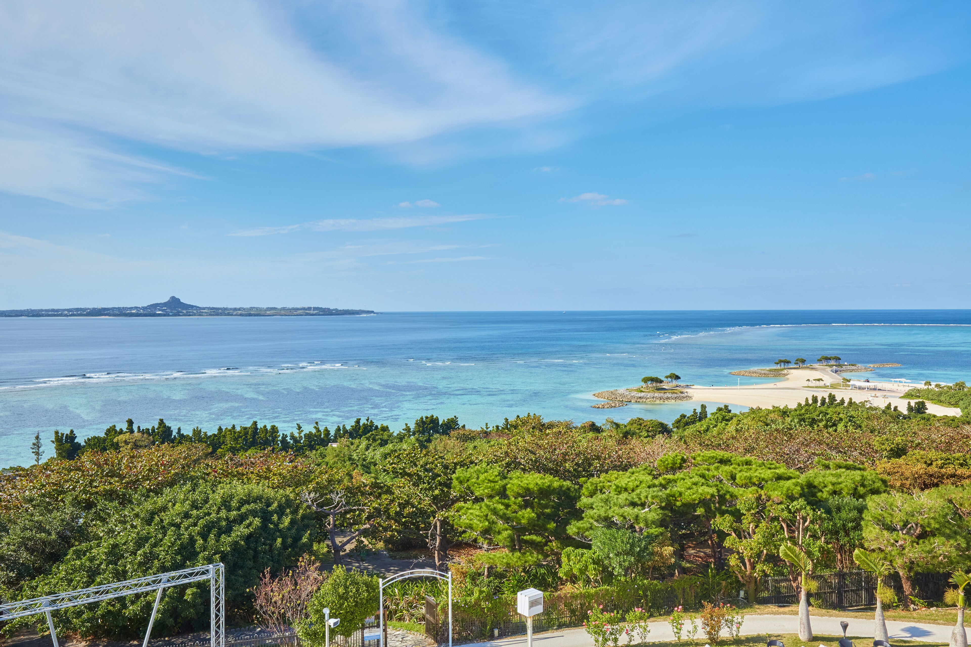 Un paysage côtier offrant une vue dégagée sur la mer, une montagne à l’horizon et une végétation luxuriante au premier plan.