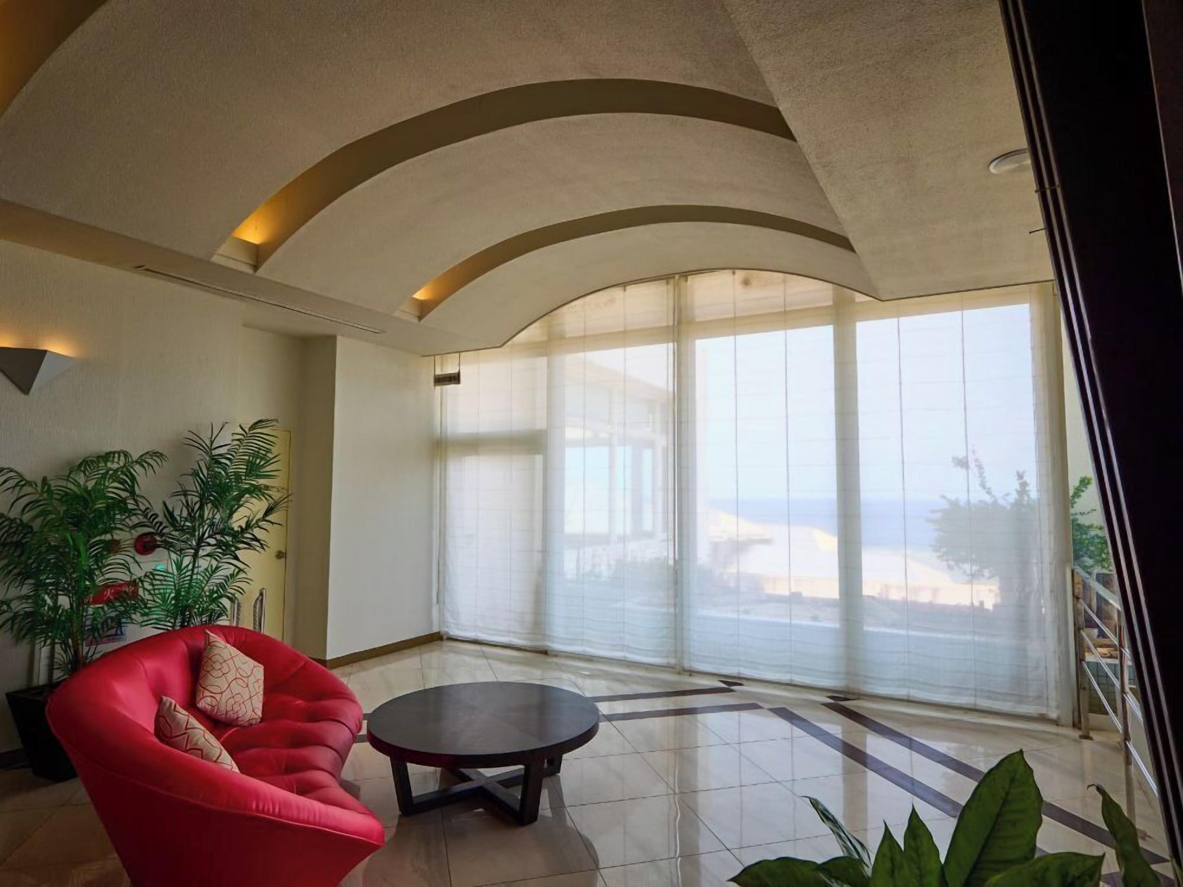 A spacious room with a red chair, a small table, and large windows offering a view.