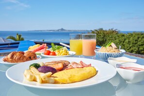 A breakfast table with croissants, eggs, tomatoes, corn, and juice, overlooking a scenic ocean view. - Royal View Hotel Churaumi - Closest to Churaumi (Motobu)