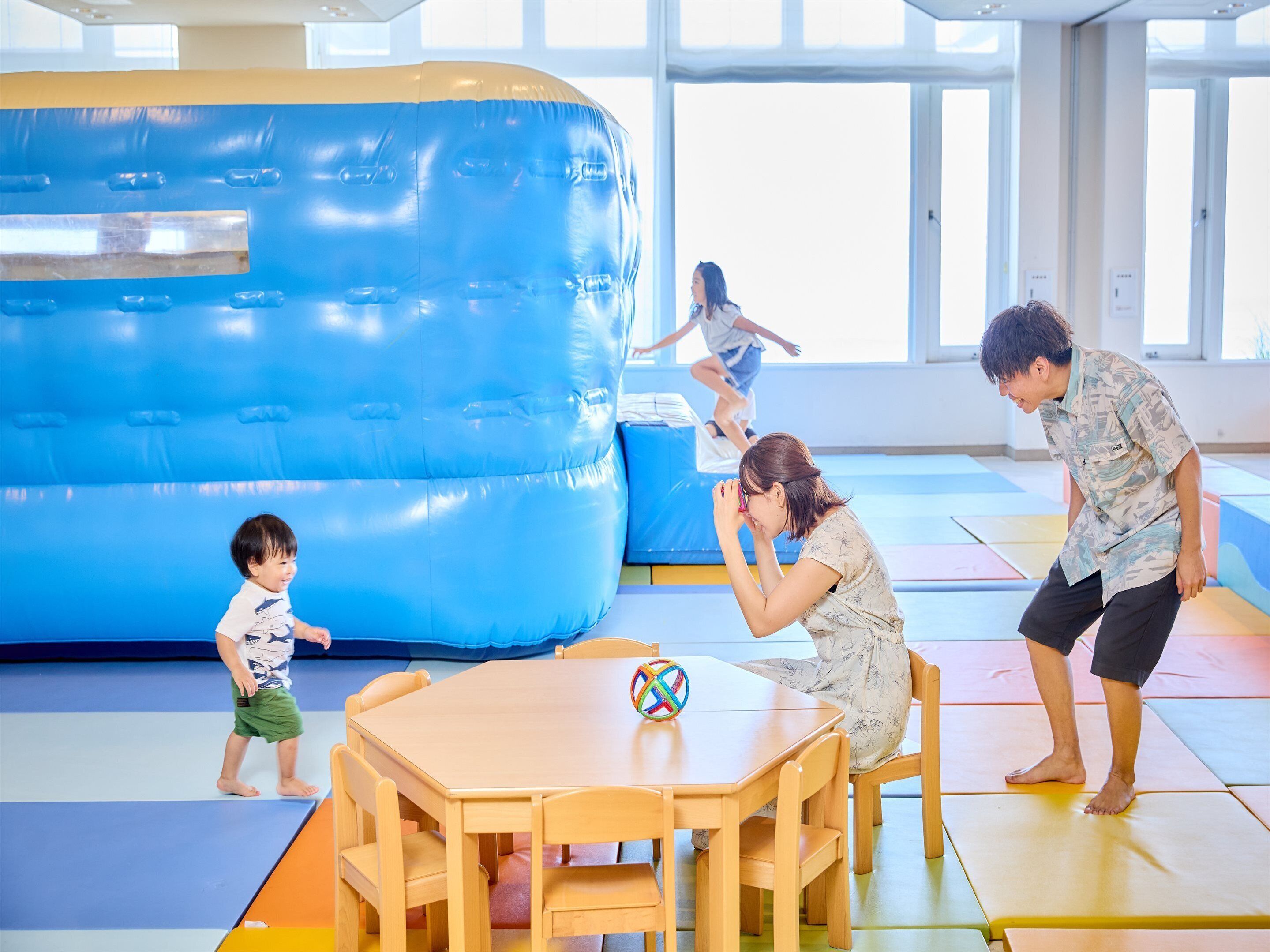 A gymnasium with padded flooring, a blue padded structure, and a wooden table with chairs.