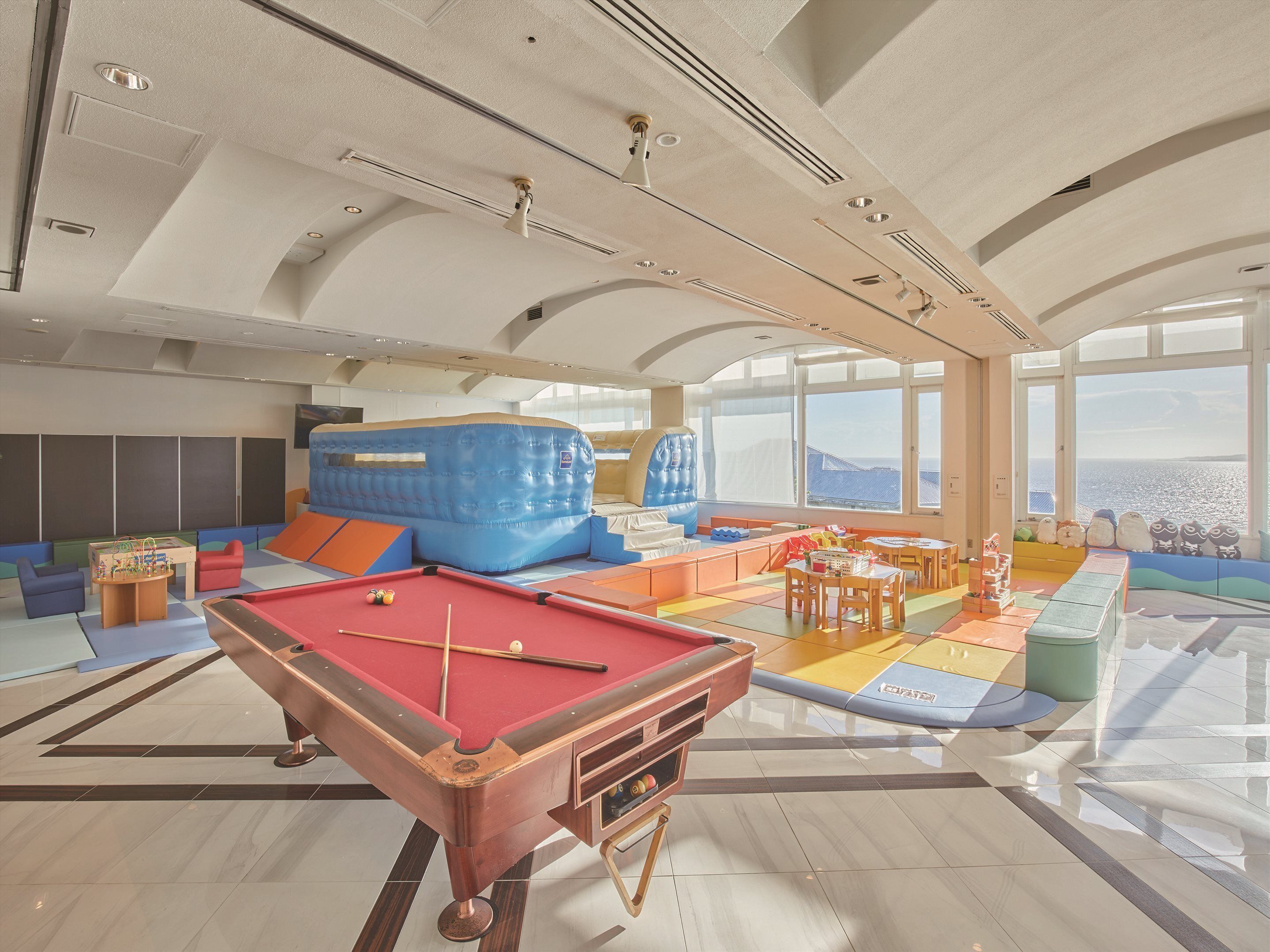 A spacious indoor area with a pool table, colorful play area, and large windows offering a view.