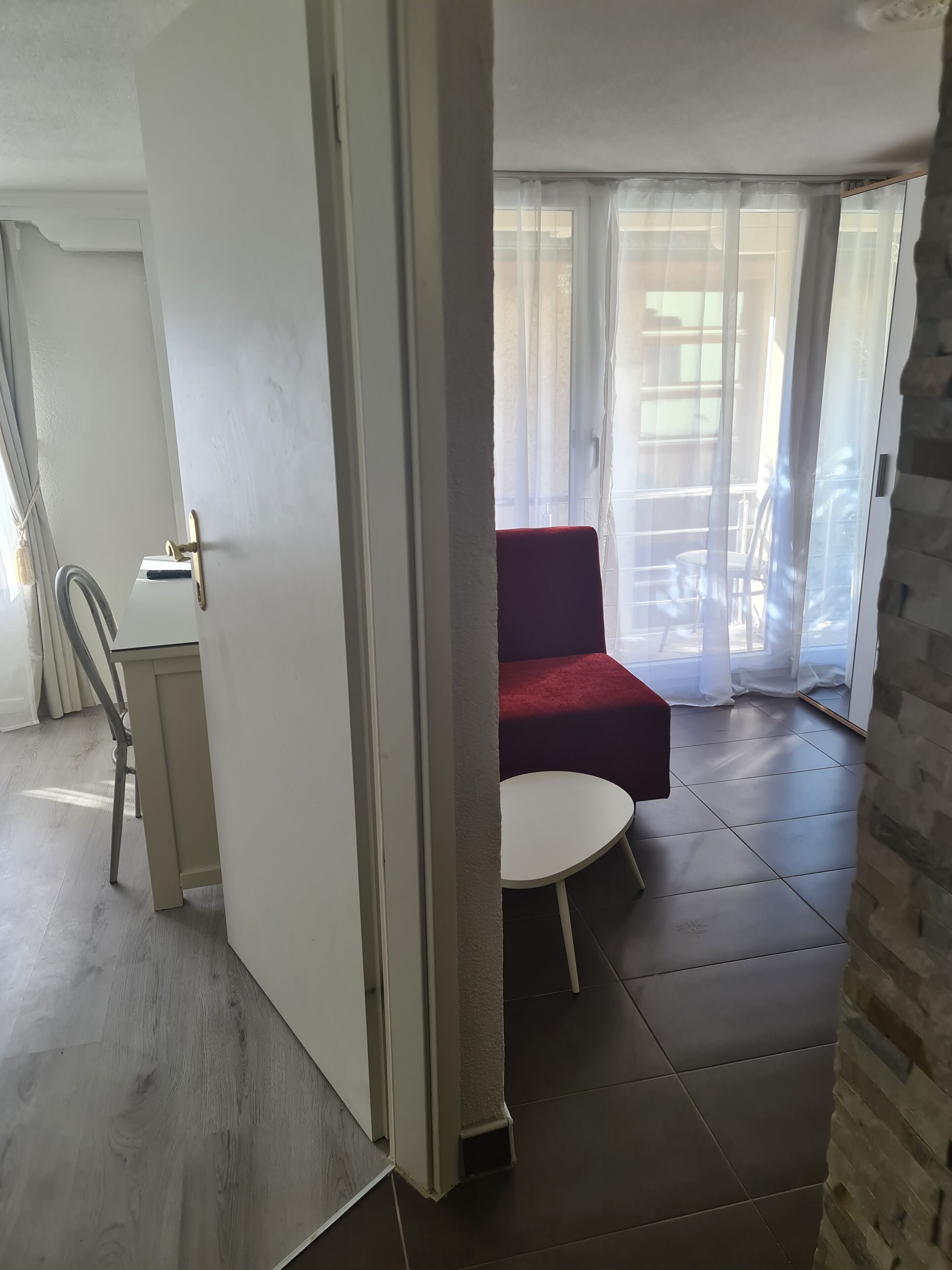 Una habitación con un sofá rojo, una mesita redonda y vistas al exterior a través de cortinas translúcidas.
