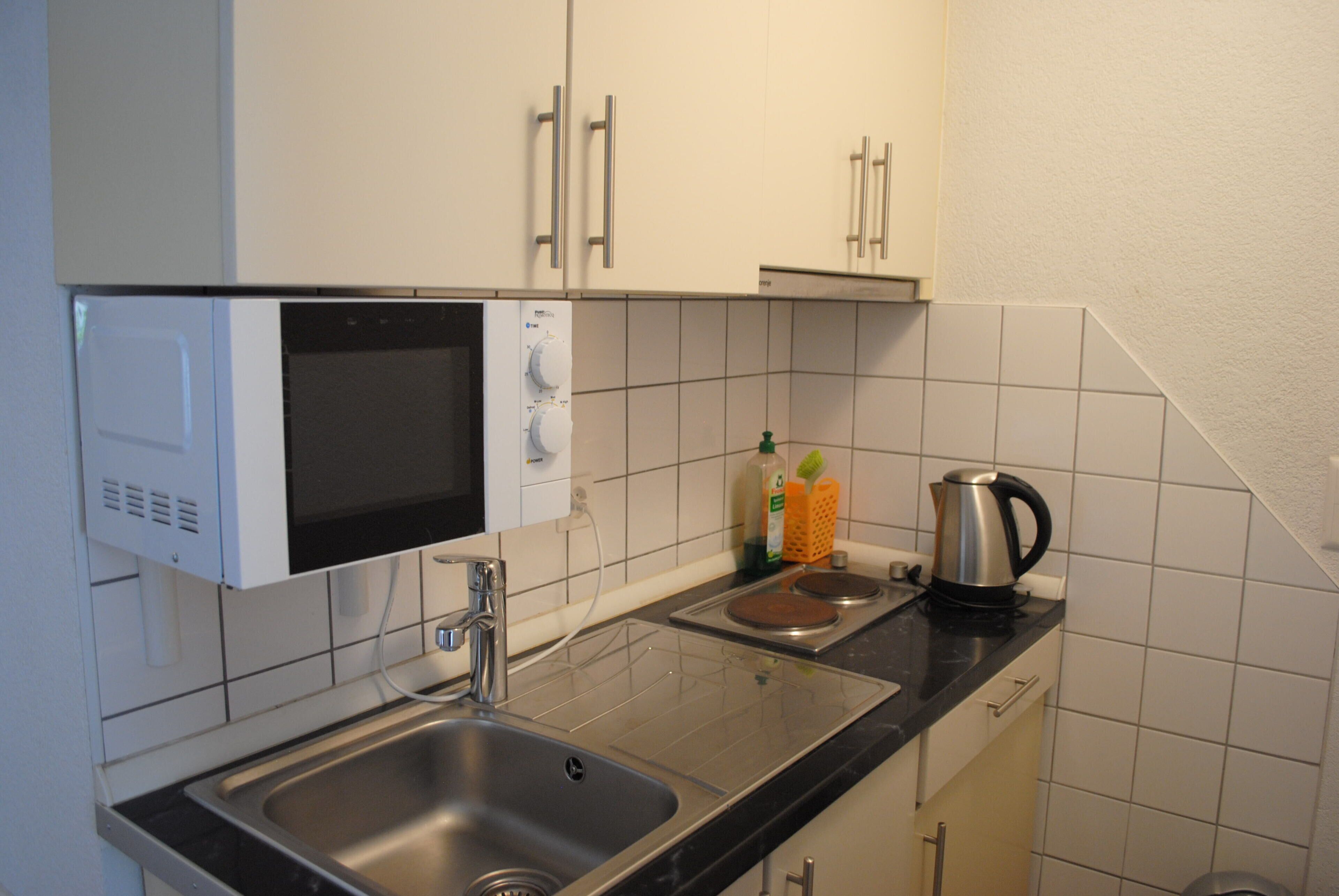 A compact kitchen with a built-in microwave, a sink, and a kettle on the countertop.