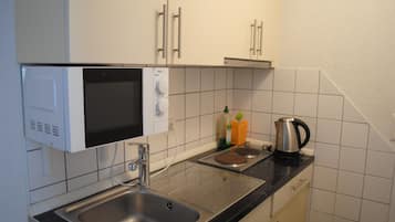 A compact kitchen with a built-in microwave, a sink, and a kettle on the countertop.
