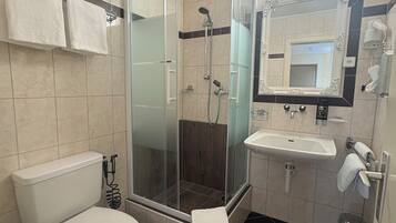 A modern bathroom with a glass-enclosed shower, a white toilet, a sink, and a mirror with a decorative frame.