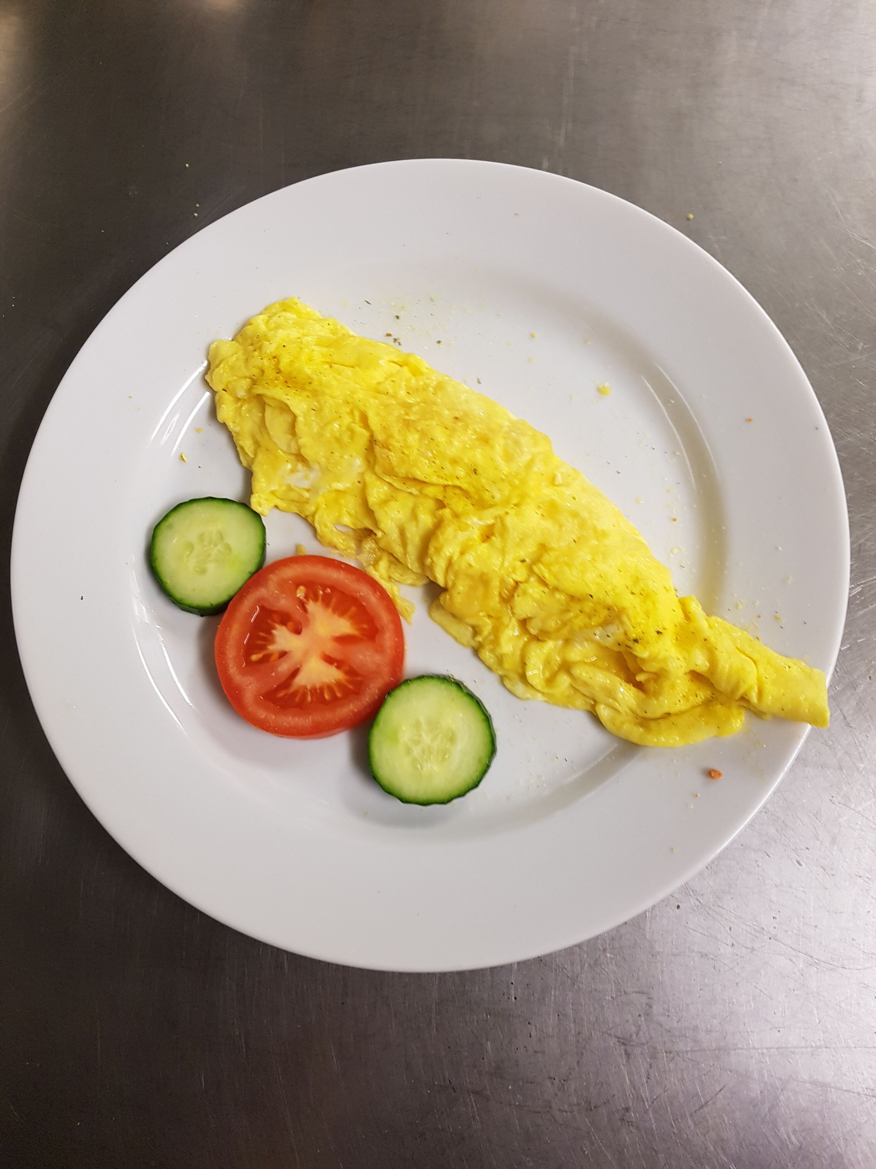 A plate with an omelette, a slice of tomato, and two slices of cucumber.