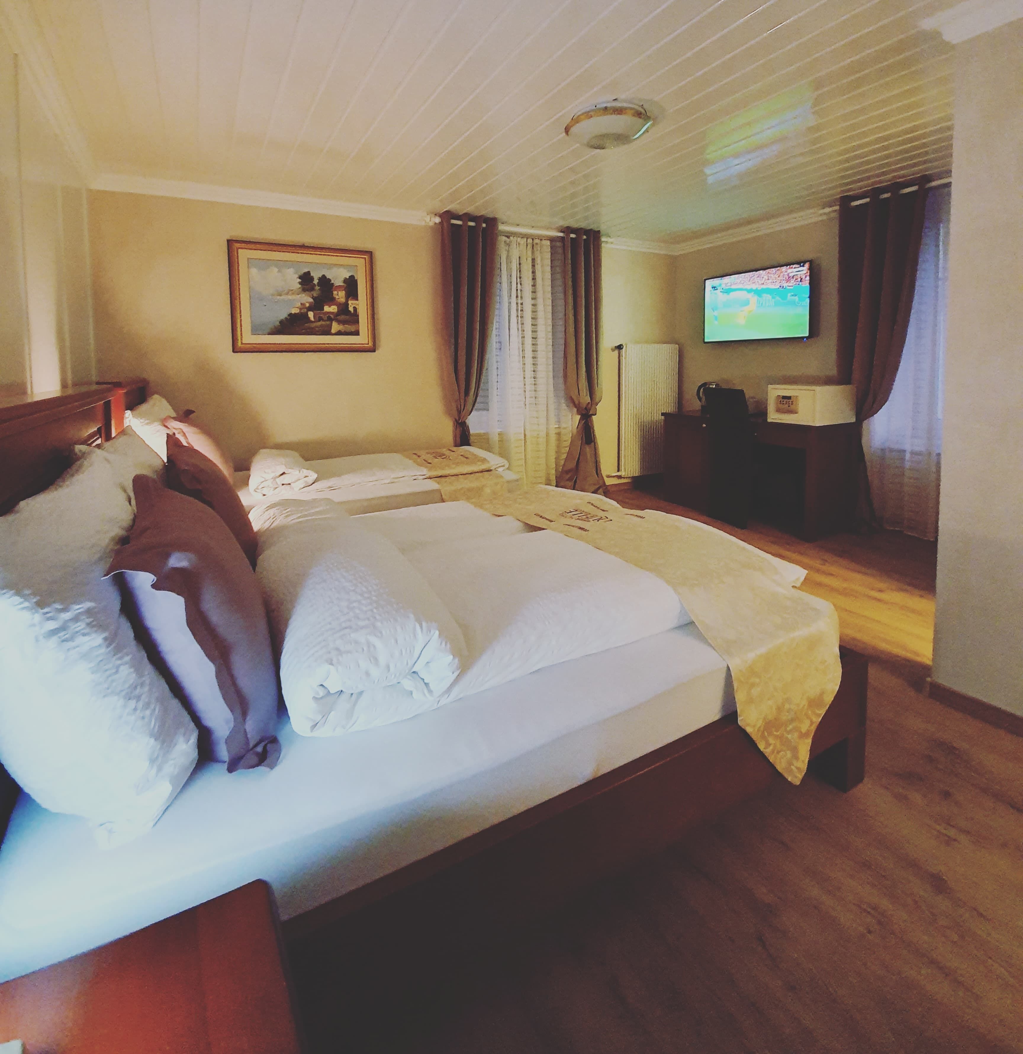 Ein Hotelzimmer mit einem großen Bett, einem Fernseher, einem Bild an der Wand und einem Schreibtisch mit einer Lampe.