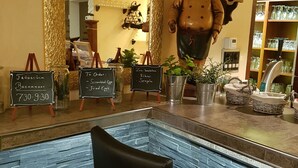 Een restaurant met een aanrecht van steen, zwarte stoelen en schoolborden waarop ontbijttijden en menu staan.