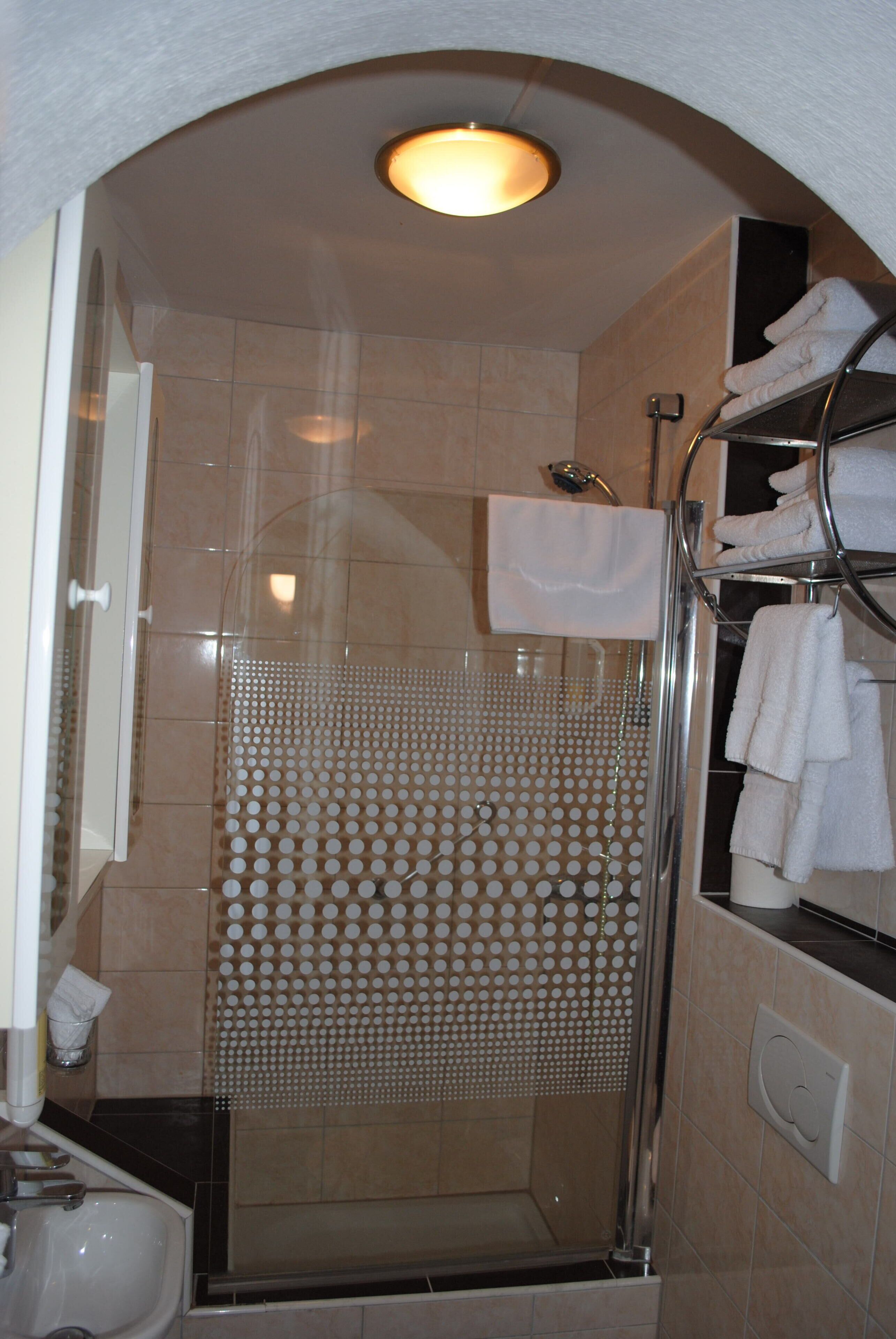 Een douche met een glazen deur, een handdoekrek met handdoeken en een lamp boven de douche.