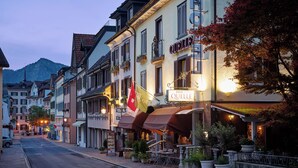 Hotel QUELLE met een naambord, een terras met tafels en stoelen, en potplanten.