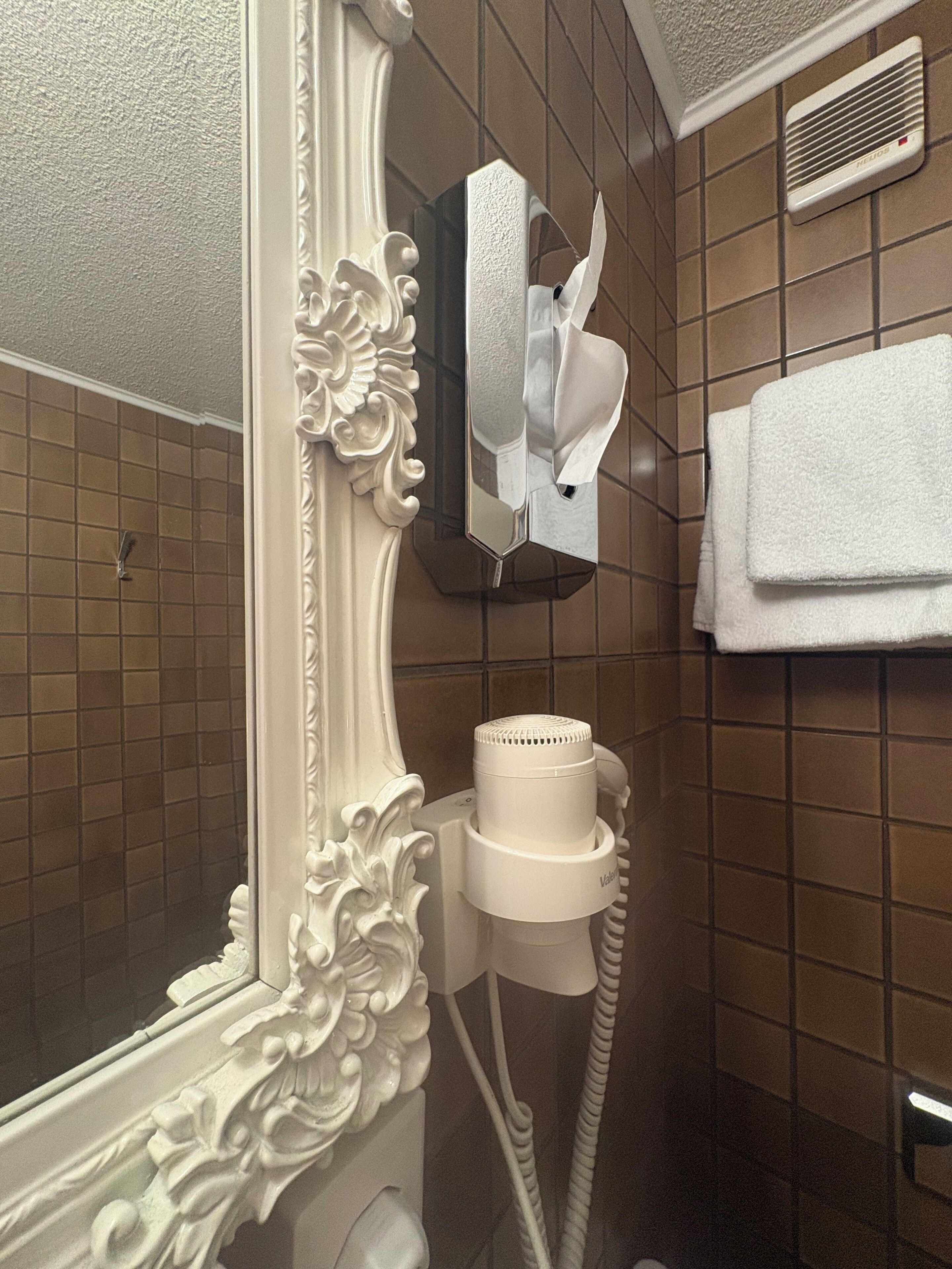 A bathroom with a white ornate mirror, a hairdryer, and a towel rack.
