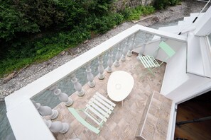 A rooftop terrace with a glass balustrade, a white table, and a green chair.