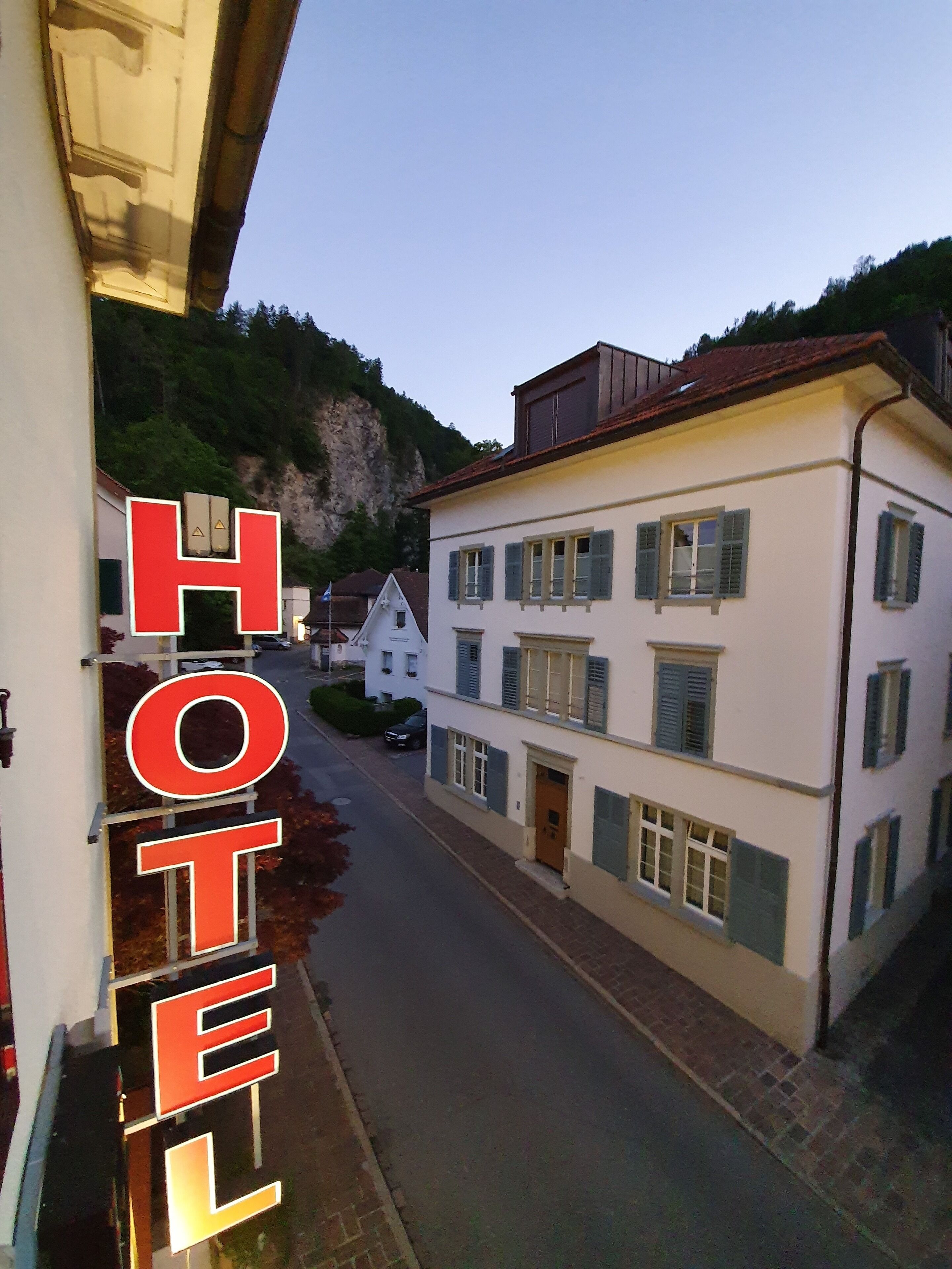 A hotel with a street view, buildings with shutters, and a mountain backdrop.