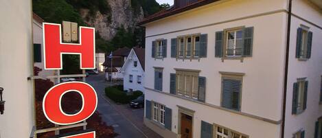 A hotel with a street view, buildings with shutters, and a mountain backdrop.