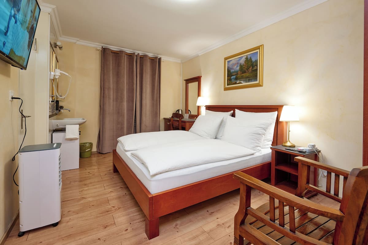 A hotel room with a wooden bed, a desk, a chair, a television, and a painting on the wall.