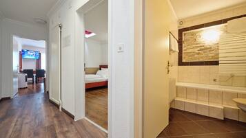Une chambre d’hôtel avec un plancher en bois, un lit, une salle de bain avec baignoire et un téléviseur dans l’espace salon.