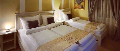 Habitación de hotel con dos camas, una mesita de noche con lámpara, un cuadro en la pared y una ventana con cortinas.