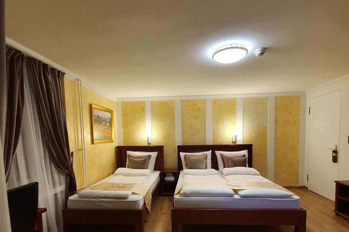A hotel room with two single beds, wooden flooring, a ceiling light, and a wall-mounted picture.