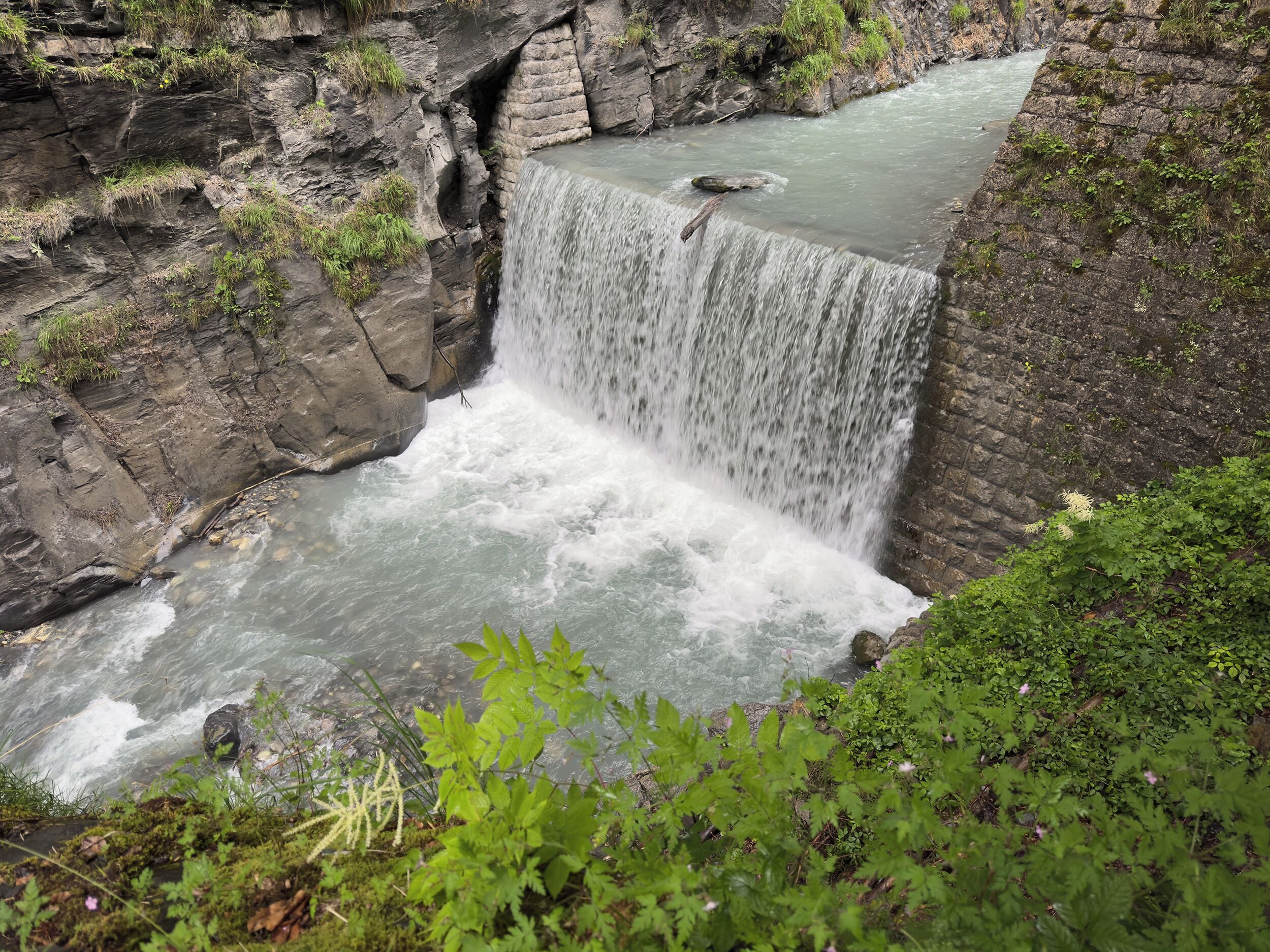 A waterfall cascading over a rocky cliff into a river, surrounded by greenery.