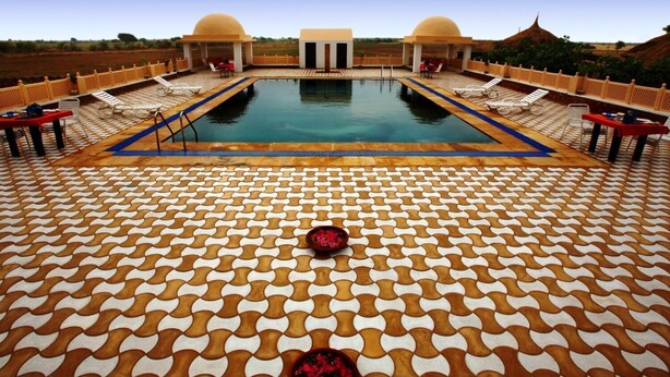 Zona de piscina con un diseño de baldosas geométricas, sillas de descanso y una piscina central.