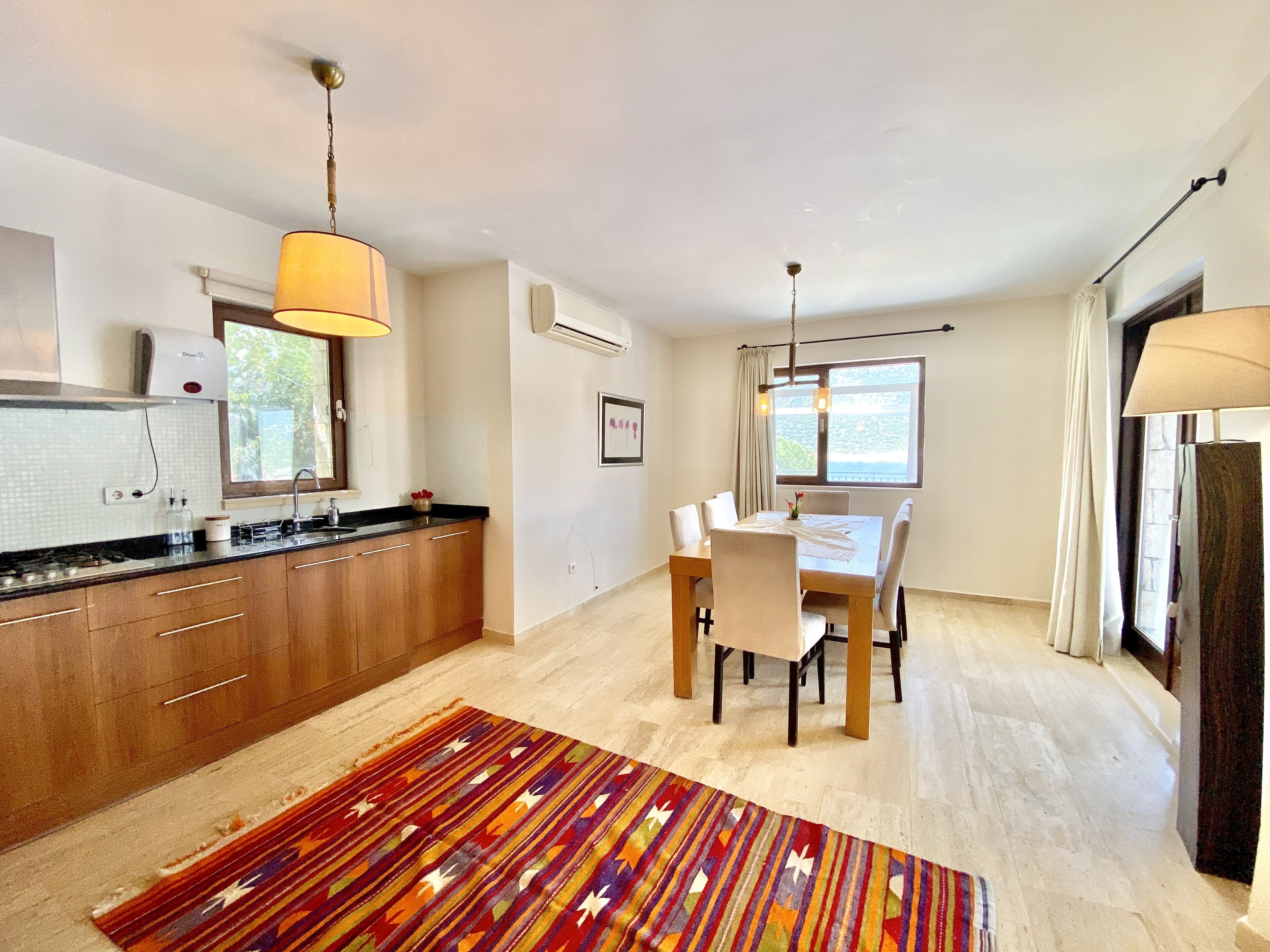 A modern kitchen with wooden cabinets, a dining table with chairs, and a colorful rug.