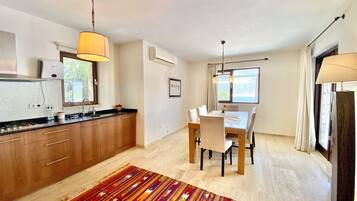A modern kitchen with wooden cabinets, a dining table with chairs, and a colorful rug.