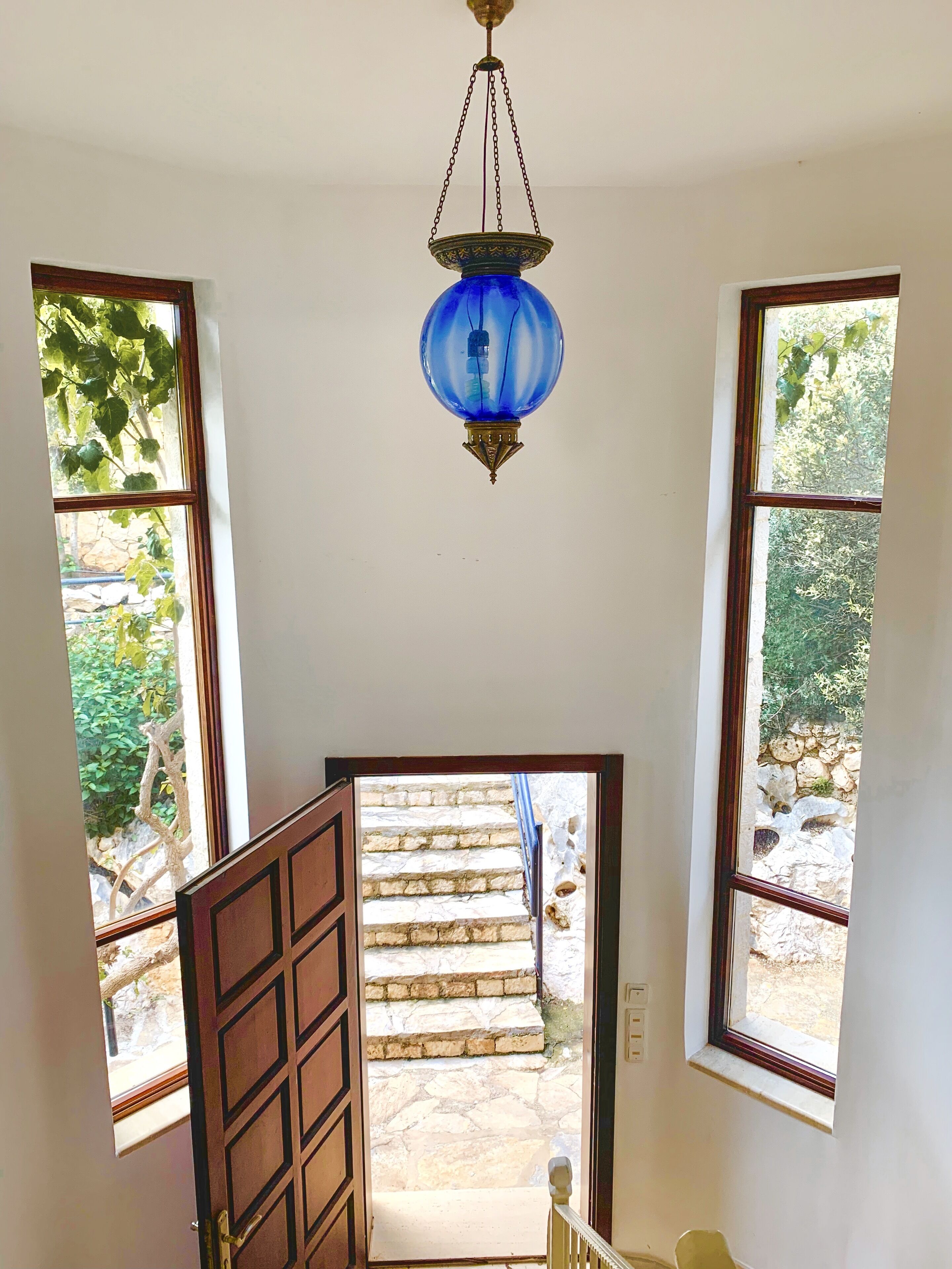 A room with a blue hanging lamp, a wooden door, and a view of stone steps leading outside.