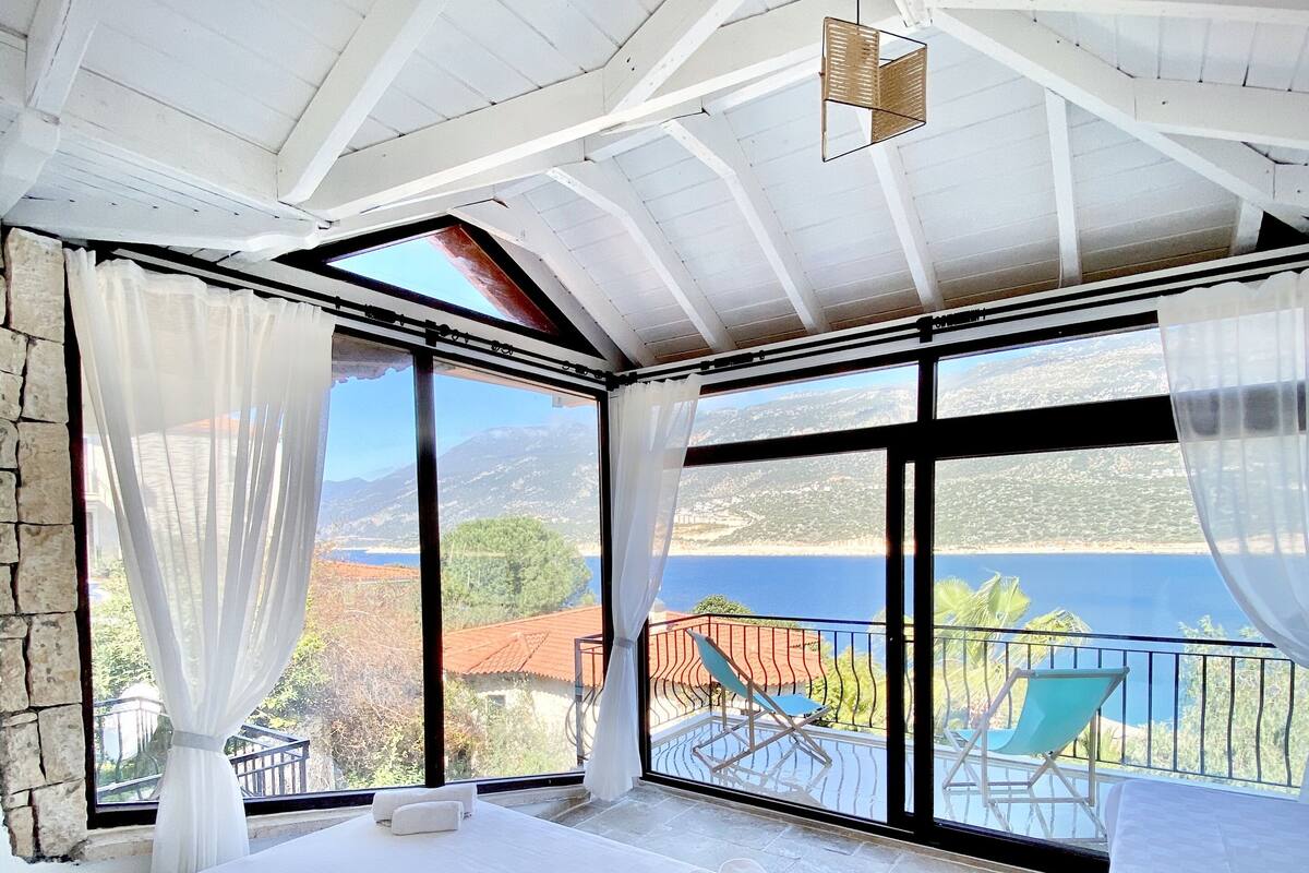 Un dormitorio con una cama grande, una cama más pequeña y un balcón con vistas al mar y a las montañas.