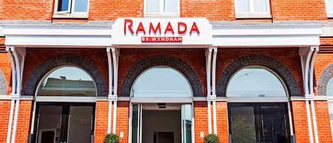 A brick building with a sign reading "RAMADA BY WYNDHAM" above the entrance.