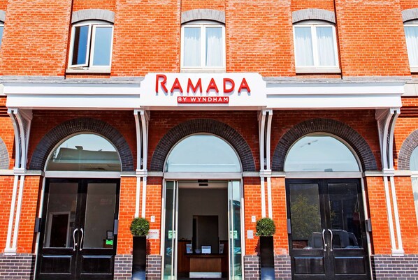 Un edificio de ladrillo con un letrero que dice "RAMADA BY WYNDHAM" sobre la entrada.