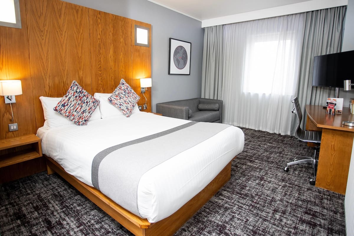 A hotel room with a large bed, a desk, a chair, a TV, and a window with curtains.
