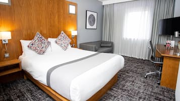 A hotel room with a large bed, a desk, a chair, a TV, and a window with curtains.
