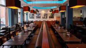 Un restaurante con largas mesas de madera, asientos tapizados en negro y lámparas colgantes.