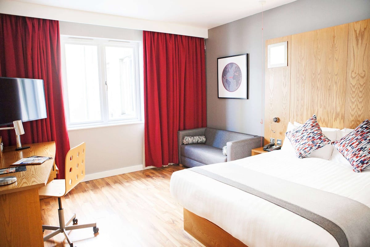 A hotel room with a large bed, a desk with a chair, a sofa, and a TV.