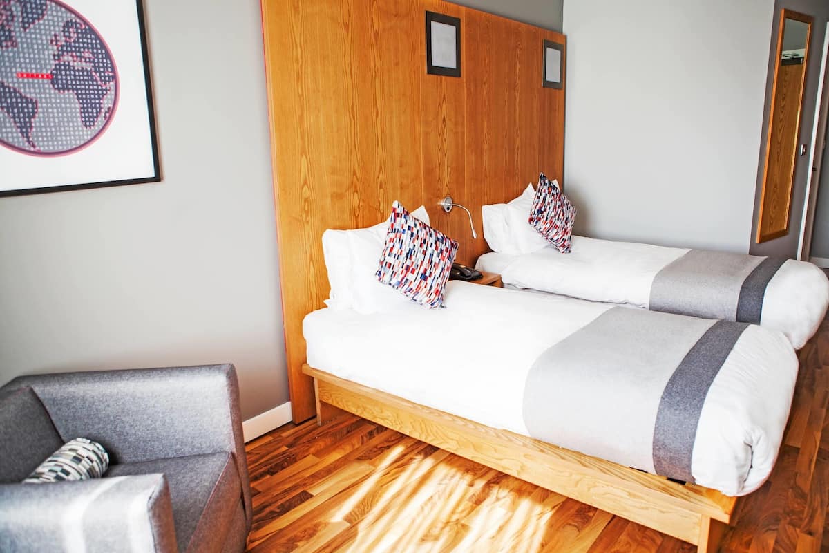 A bedroom with a wooden bed, two pillows, a grey armchair, and a framed picture on the wall.