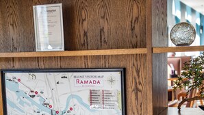 Una vitrina de madera con un mapa titulado 'Belfast Visitor Map Ramada by Wyndham', un cartel sobre la propiedad Ramada y una planta en maceta.