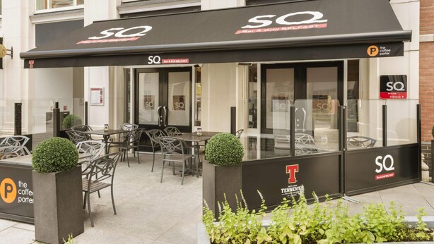 Un área de estar al aire libre con mesas y sillas, un macetero con café y un letrero para SQ Bar & Grill Belfast.