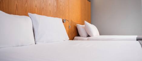 Una habitación de hotel con cabecera de madera, cama con ropa blanca y mesita de noche con lámpara.