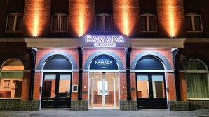 Un edificio con un letrero que dice "RAMADA BY WYNDHAM" y una entrada amplia con puertas de vidrio.
