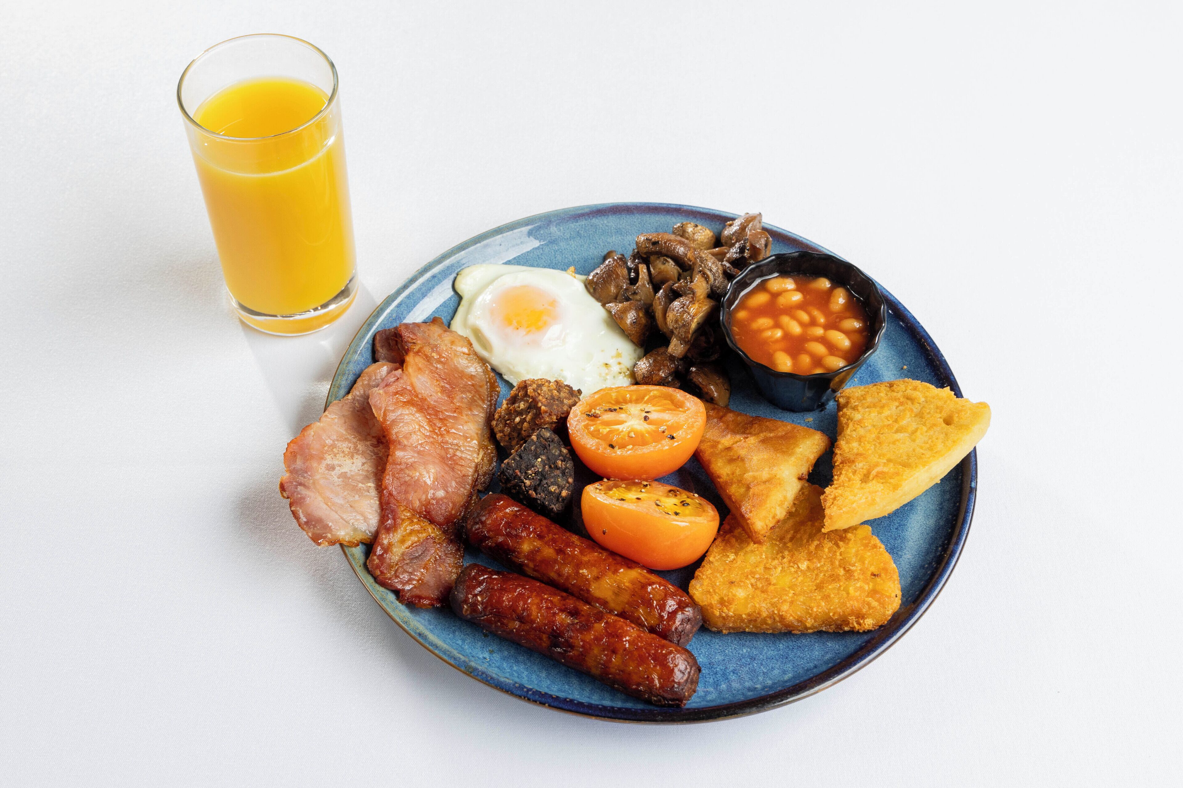 Een bord met ontbijtproducten, zoals spek, worstjes, eieren, champignons, bonen en toast.