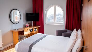 Una habitación de hotel con cama, escritorio con computadora, televisión y ventana con cortinas.