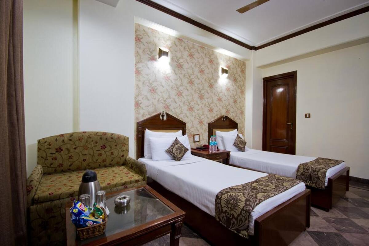 Habitación de hotel con dos camas individuales, un sofá, una mesita con aperitivos y un detalle decorativo en la pared.